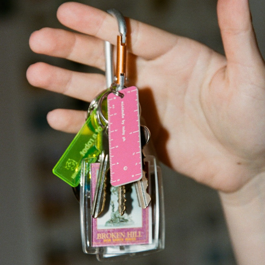 Hand holding a keychain with various keys and a pink ruler against a blurred background