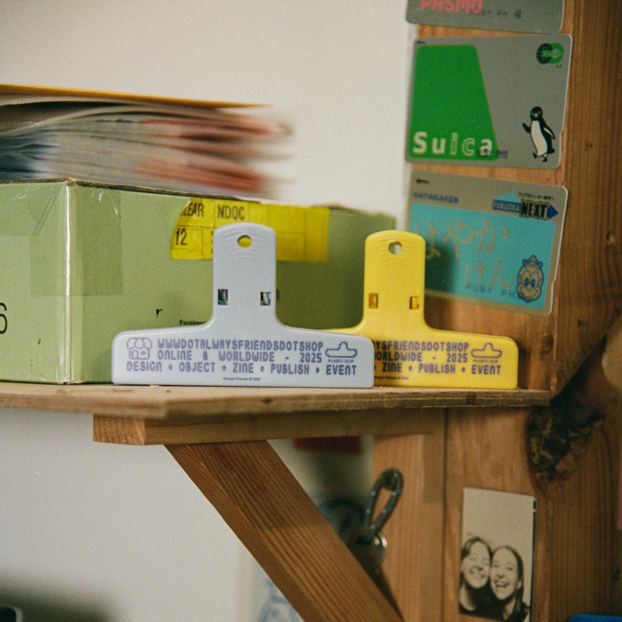 Wooden shelf with various items including a box, tools, and small signs on a white wall.