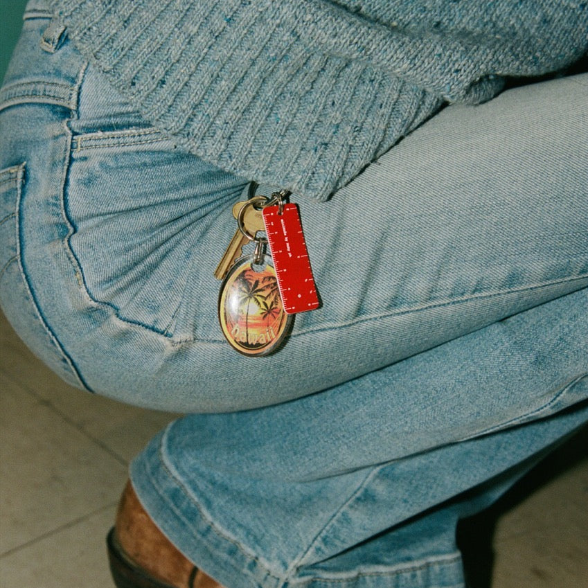Person wearing blue jeans with a keychain attached, sitting on a tiled floor.