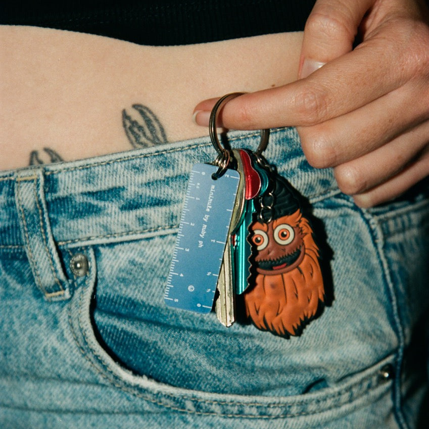 Person holding a keychain with an owl design and a ruler, wearing blue jeans.